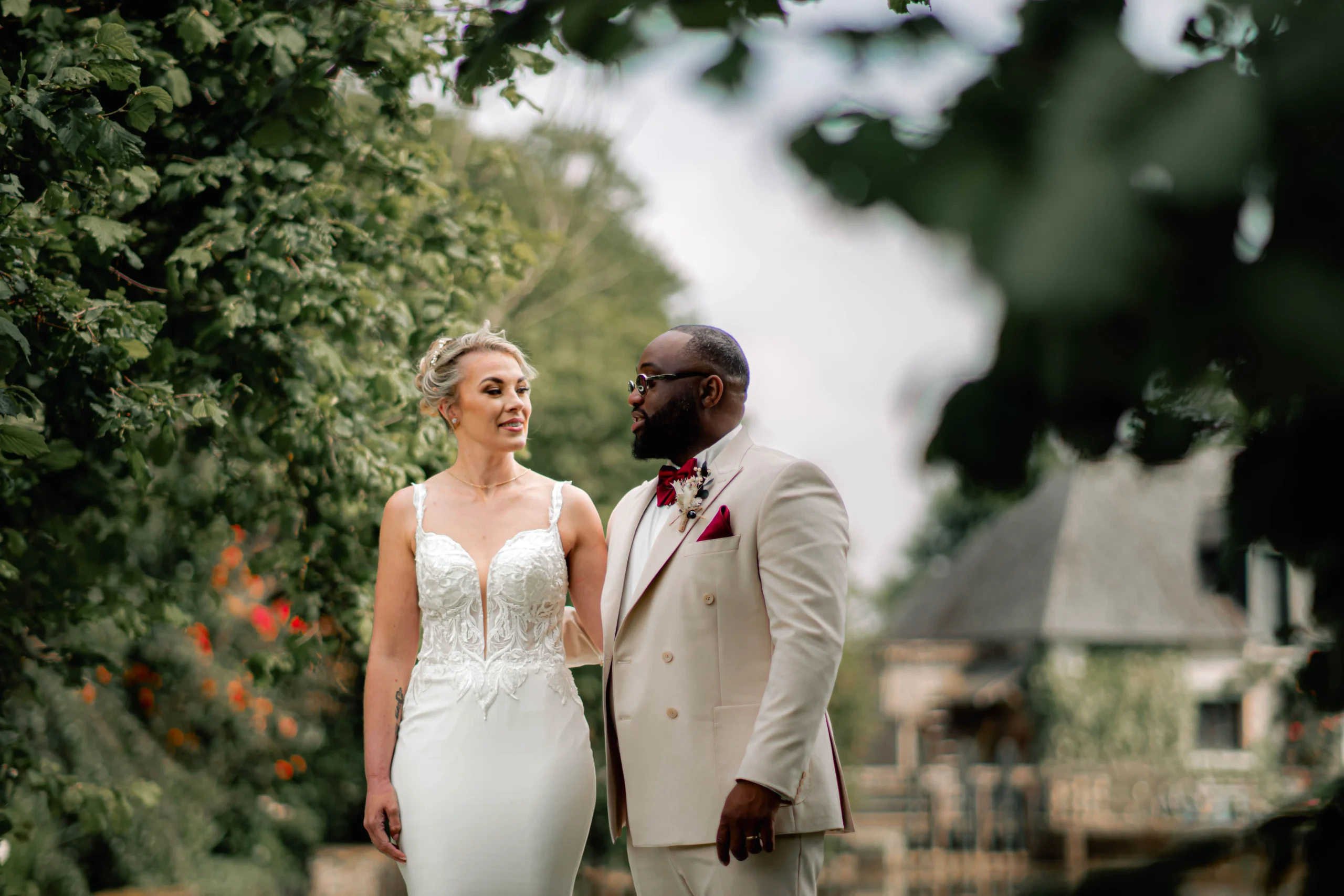 Bride and groom share a quiet moment on a garden path during couple portraits, with a stone cottage softly blurred behind them