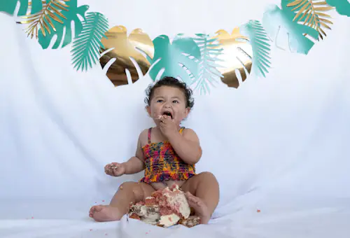 Baby girl enjoying a cake smash session in a colorful tropical-themed studio setup